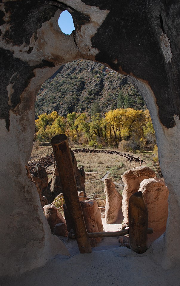 looking out a small carved doorway a stone pueblo and golden trees can be seen