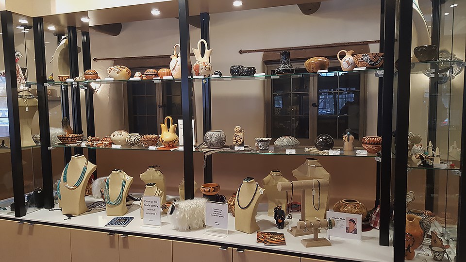 A display case with colorful beaded jewelry and brown, red, grey, and black clay pottery.