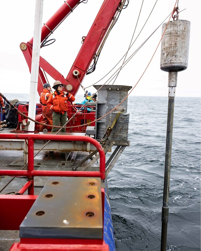 Two crew members stand next to the crane at the back of the ship.