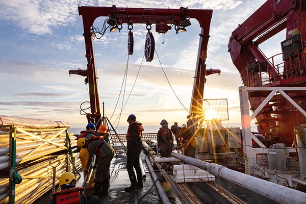 Crew members stand on the desk with the sun setting in the background.