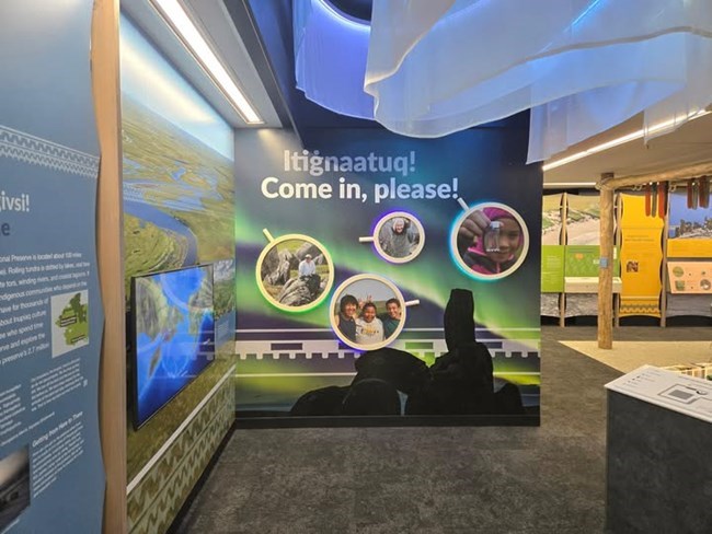 Entrance to the Heritage Center with aurora imagery and the words, "Itignaatuq! Come in, please!"