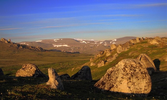 A view of the granite tors in Hot Springs Valley in vivid sunset colors, with green tundra, and patches of snow on distant mountains.