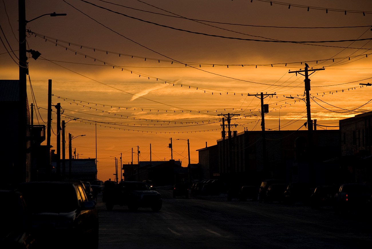 The sun rises behind a street lined with buildings