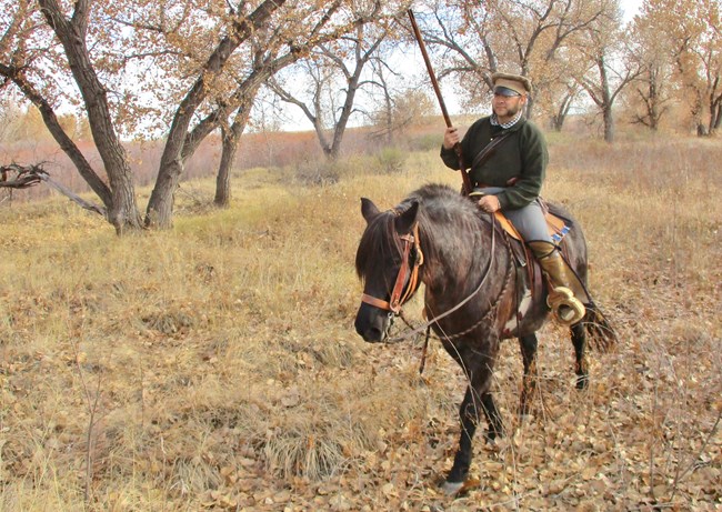 Man in living history dress rides horse on high grass trail in fall