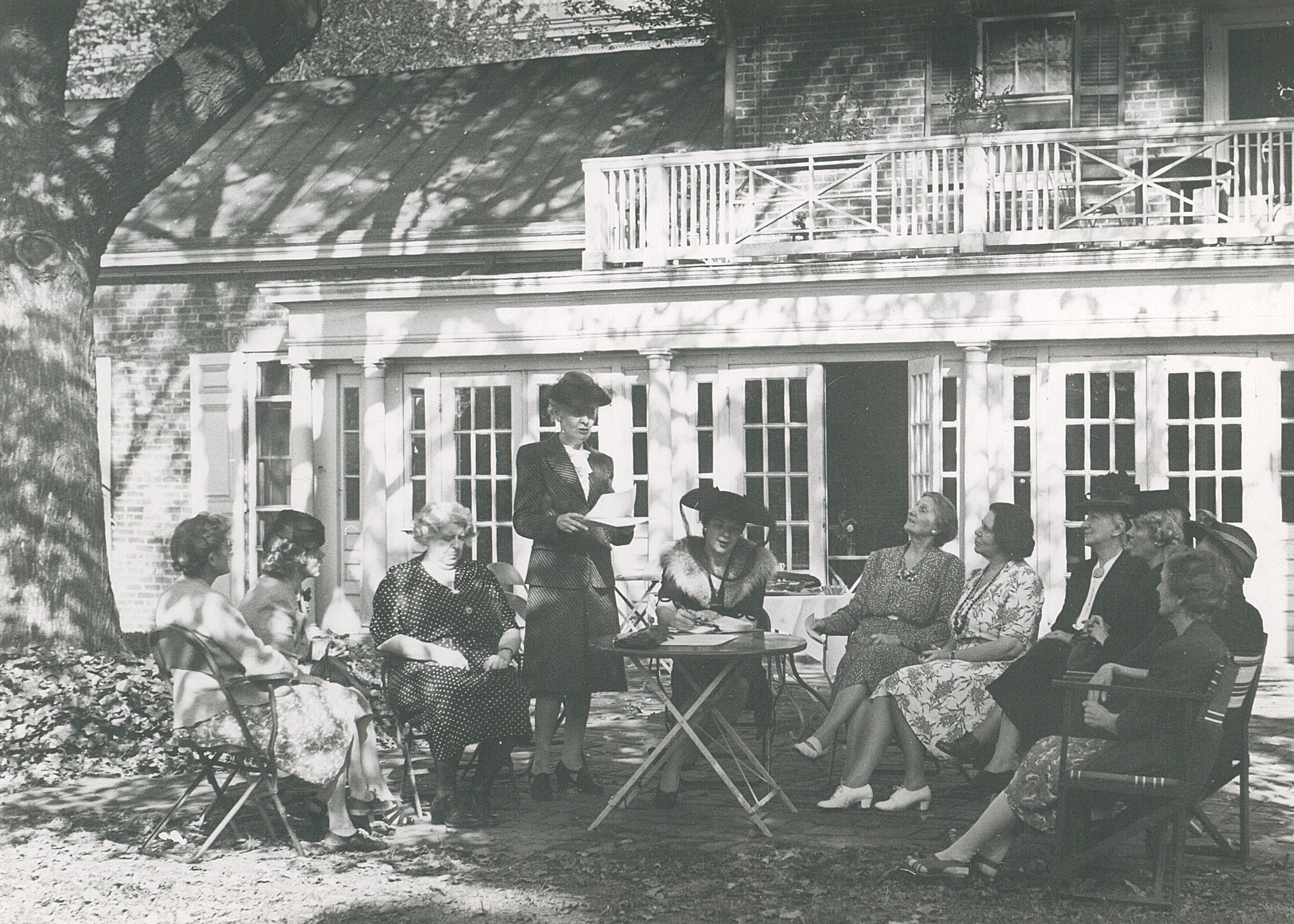 Ten women seated and one standing outside Belmont House for meeting