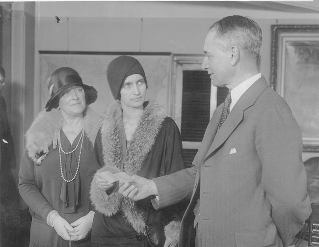 Man handing check to woman in hat while another woman looks on