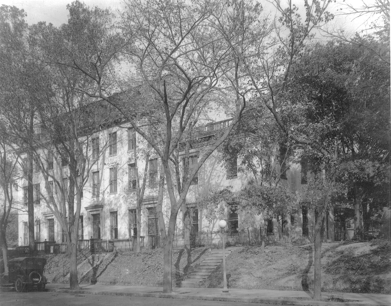 Four story white brick row building with four entrances and mansard roof