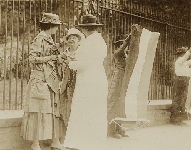 A policewoman approaches two suffragists protesting at the White House