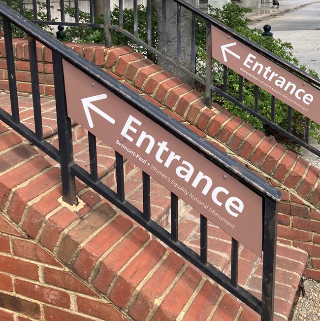 Brown directional entrance signs on railings of outdoor brick staircase