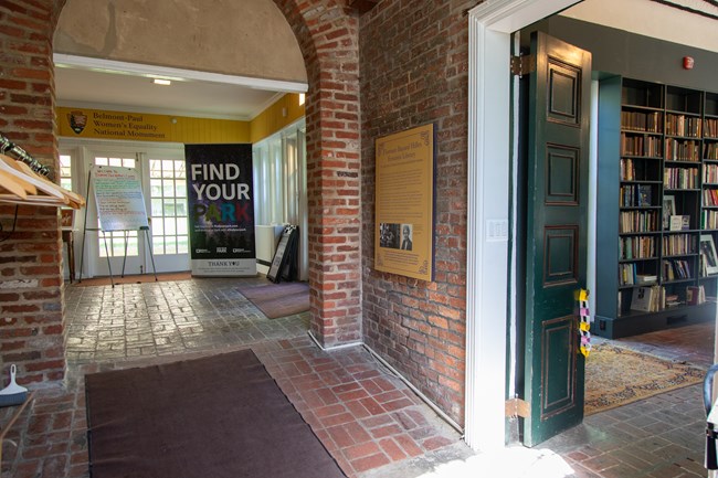 A brick ramp with a rug leading down to the open door of a room lined with books.