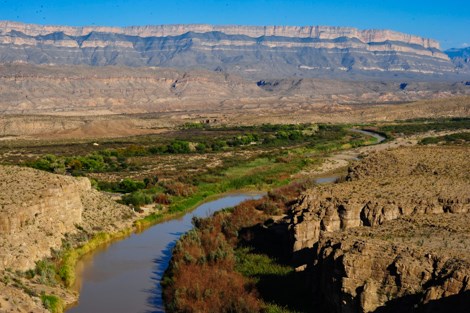 A mountain range composed of vertical cliffs of limestone dominates a desert scene above the Rio Grande.