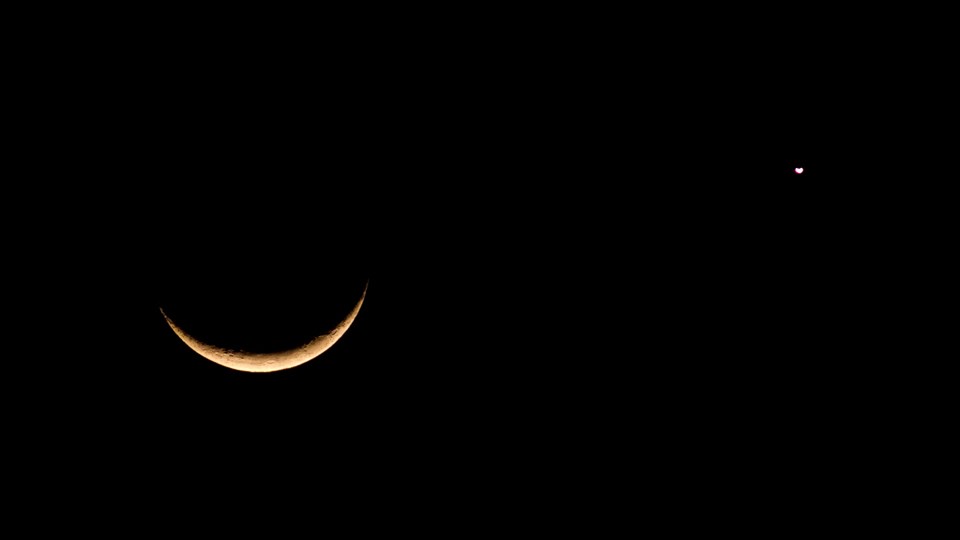 A slight crescent moon is lit from the bottom; a planet nearby is similarly lit.