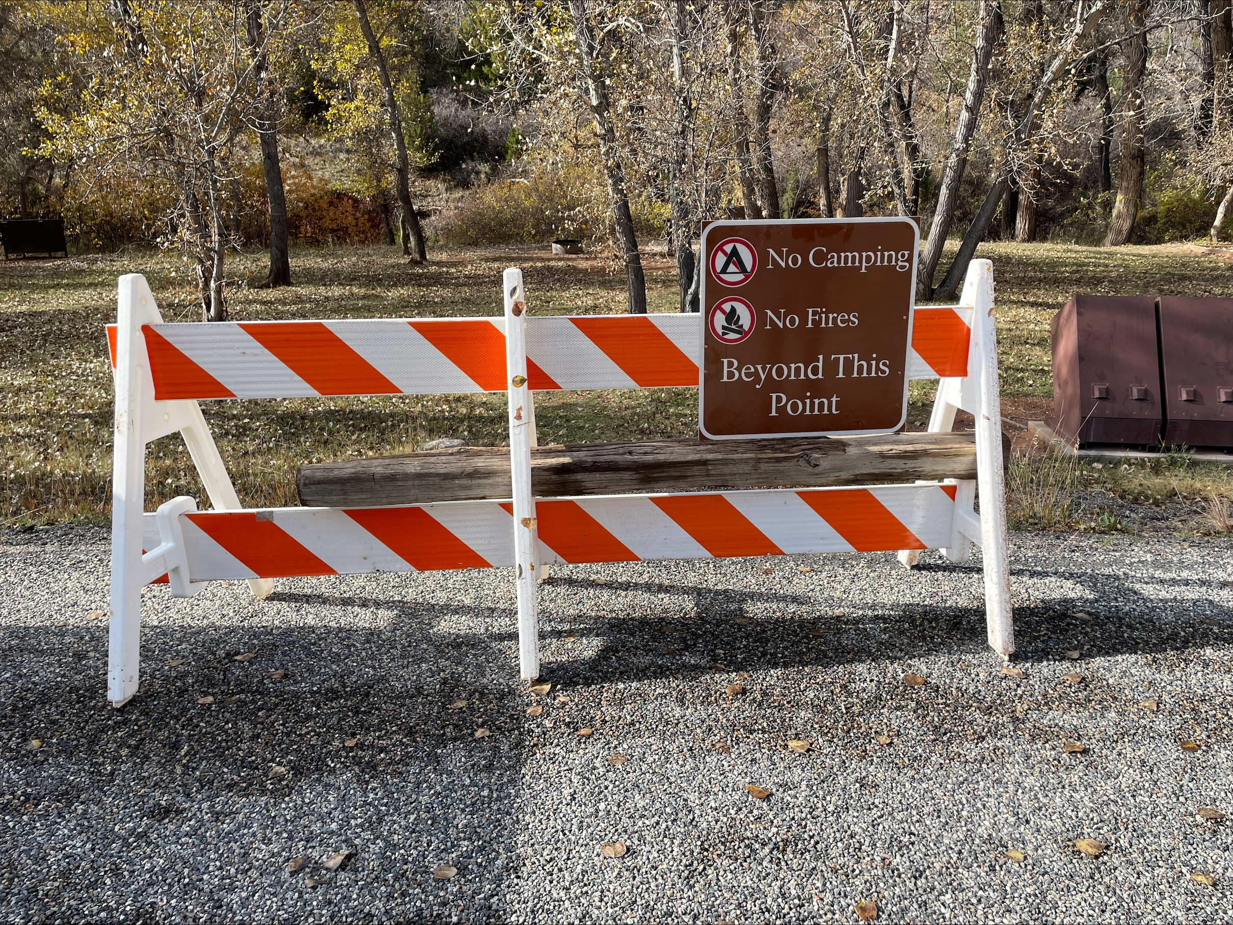 A orange and white barricade style fence with a brown park sign that reads "No Camping, No Fires, Beyond this Point" stands in front of the Trail Creek Campground Tent Camping Area.