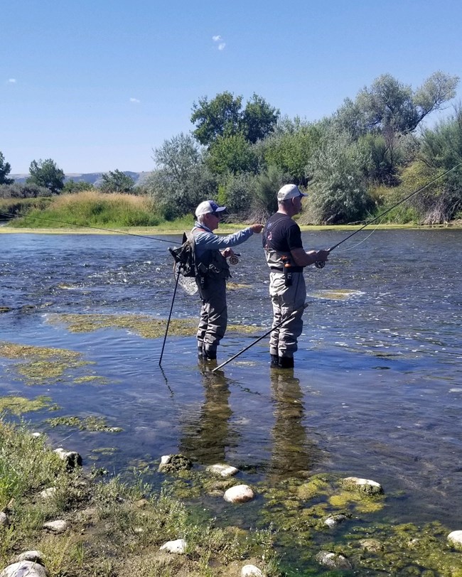 Two fisherman standing in Bighorn River with fly fishing gear.