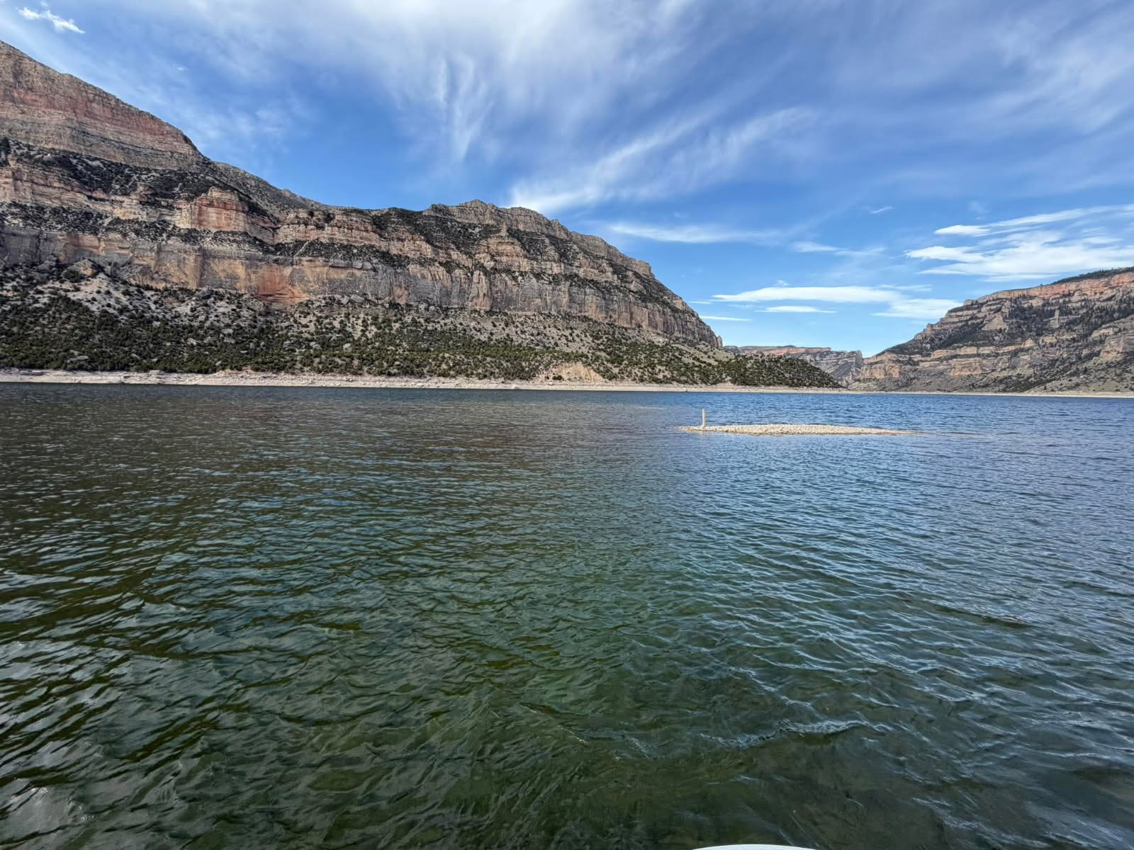 A rocky sandbar sticks out from the blue water of Bighorn Canyon with canyon walls lining the water.