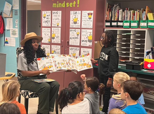 A ranger sits reading a book in front of a group of students.