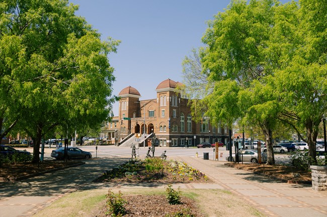 A brick church with domes is seen through trees on either side.