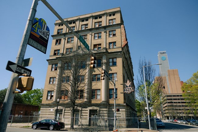 A multi-story stone building with a Masons symbol stands on a street corner.