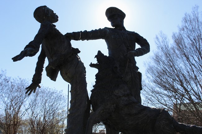 A statue of a police officer grappling with a child while a dog attacks the child.