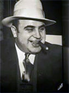 A portrait of Al Capone wearing a hat and holding a cigar in his mouth.