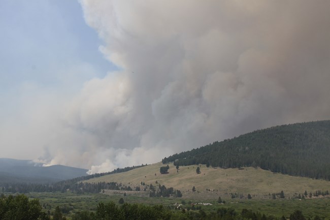 Large plumes of gray and white smoke billow up toward the sky from behind Battle Mountain.