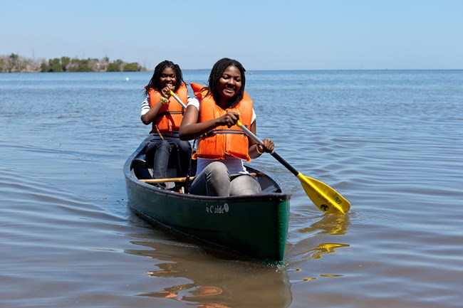 Two girls wearing orange life vests paddling in a canoe