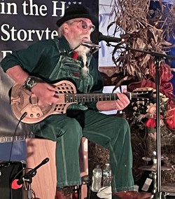 A man sitting down playing an instrument singing on stage.
