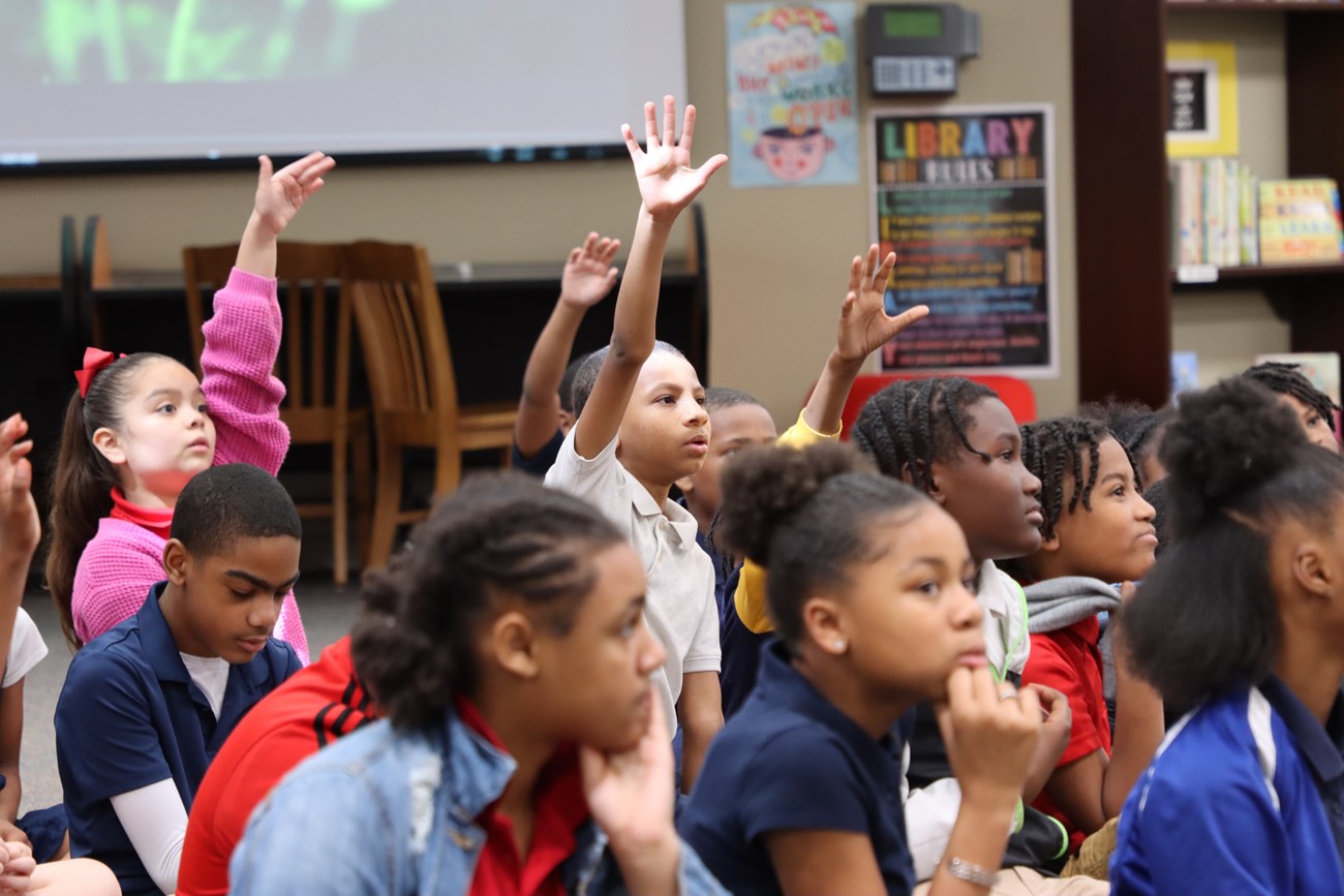 seated students raise their hands during a classroom program