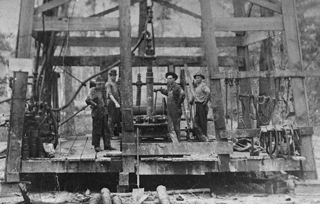 historic photo of oil workers standing beneath a derrick