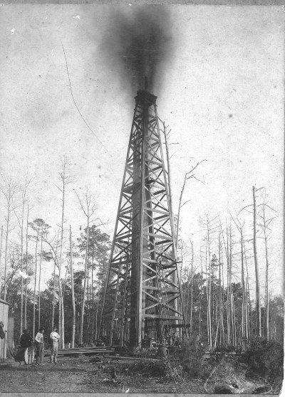historic photo gushing oil derrick with workers standing nearby