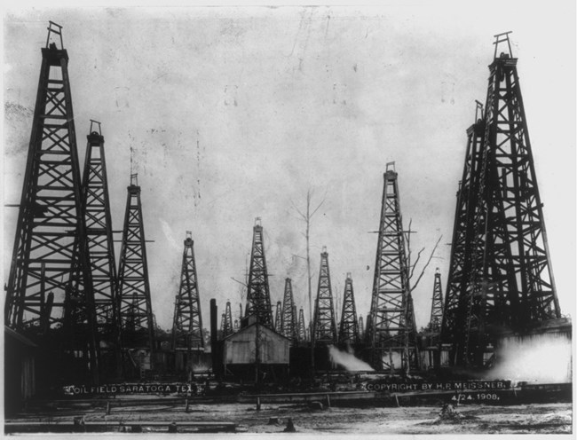 historic black and white photo of over a dozen wooden oil derricks in the Saratoga Oil Field.