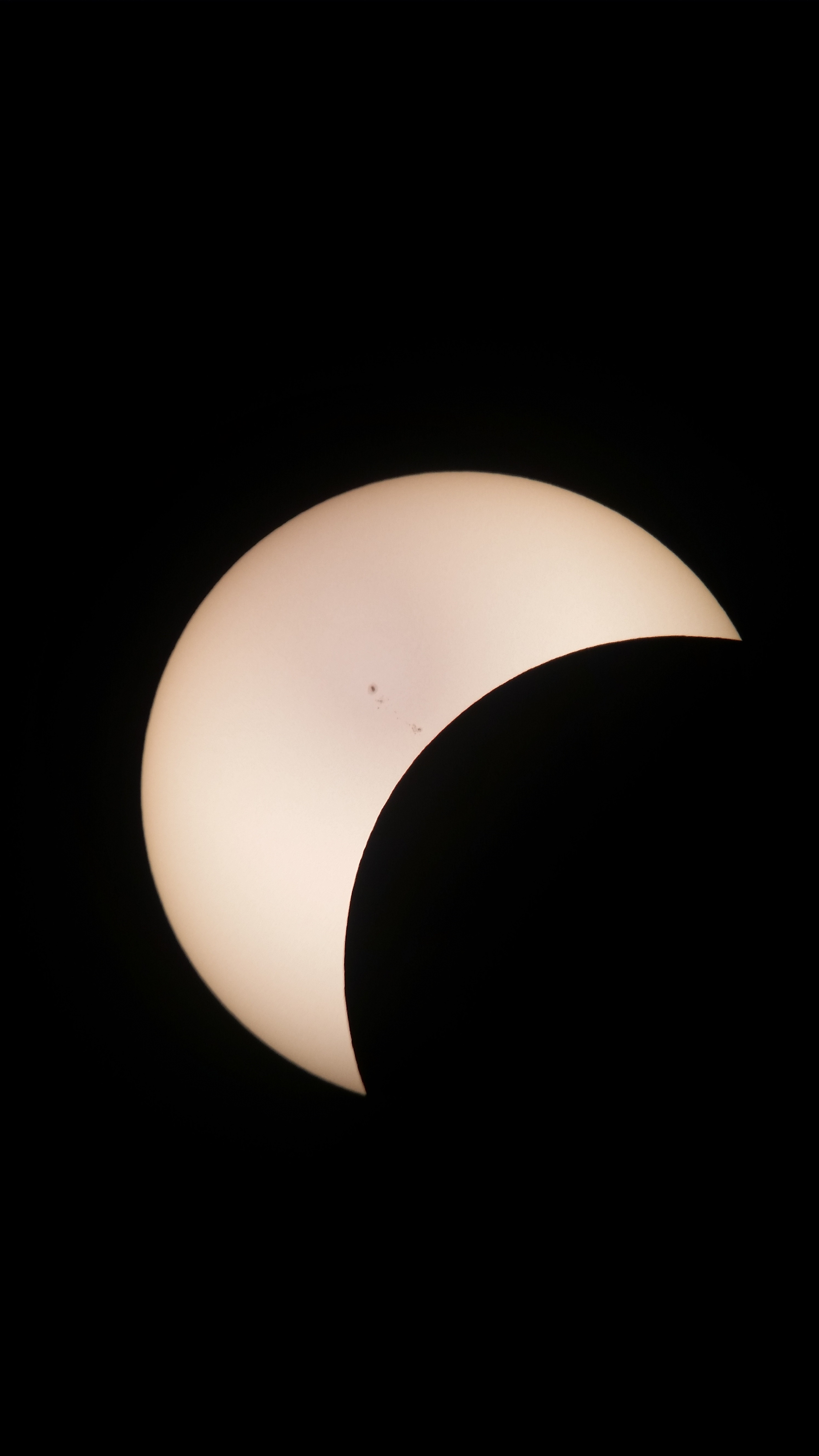 a solar eclipse showing a pale yellow disc of the sun in a crescent shape as it is eclipsed by the moon.