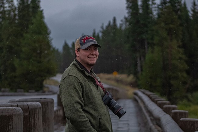 a man with a large digital camera hanging around his neck, standing outside during a light rain.