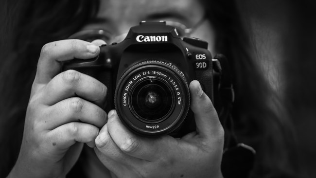 black and white photo of a person aiming their camera right into our view