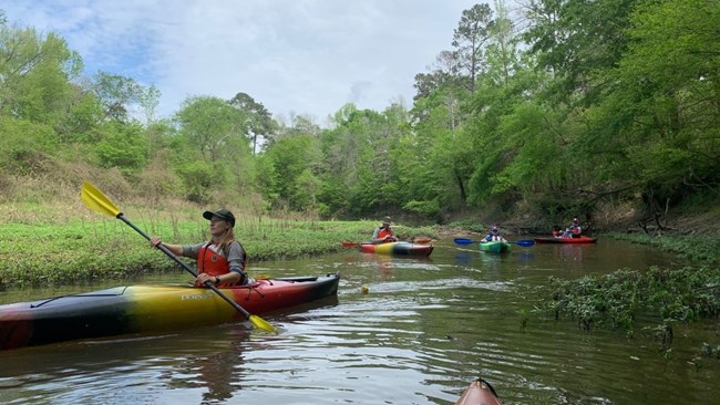 park ranger and people paddling kayaks on a creek