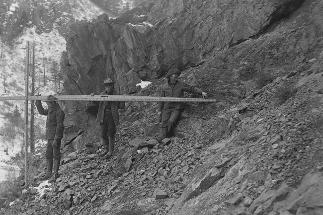 Historic image of three men with surveying equipment alongside a canyon rim.