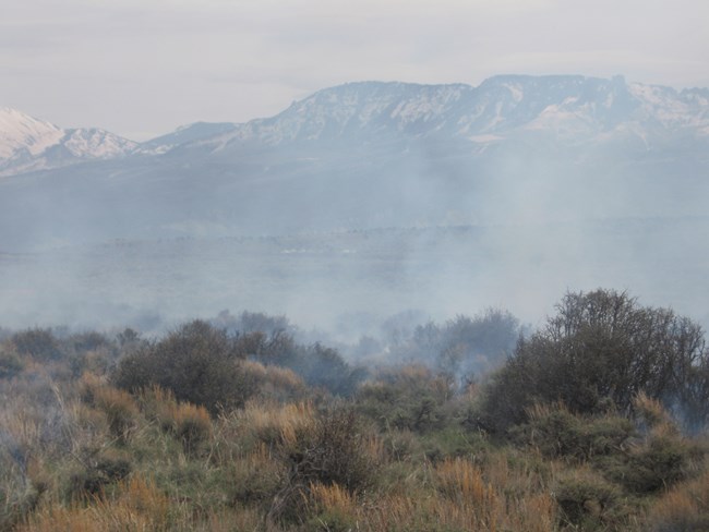 Hazy sky and some smoke from a localized prescribed burn are in the foreground. Mountains are barely visible in the background.