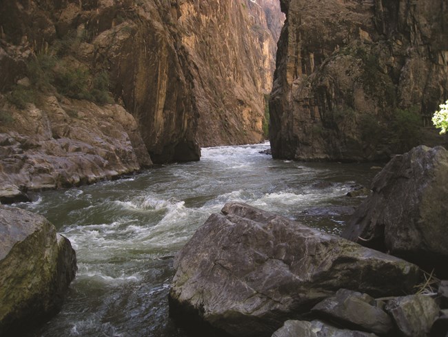 River cutting through a dark canyon. Rocks and rapids are visible.