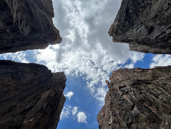 Image of a perspective looking up at a steep, dark canyon. The canyon can be seen in each corner of the image.