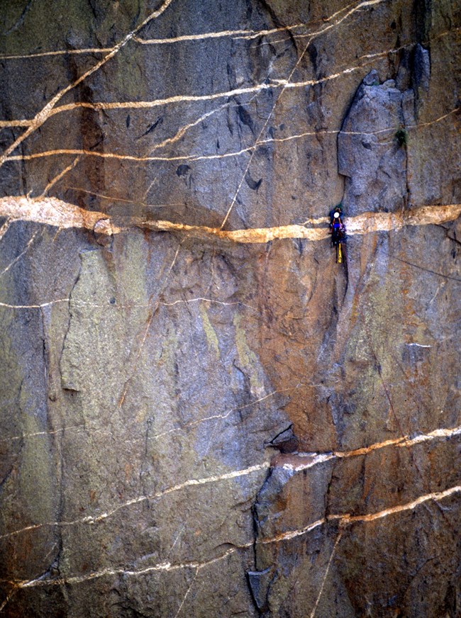 A climber going up a large crack on a wall with different color rock