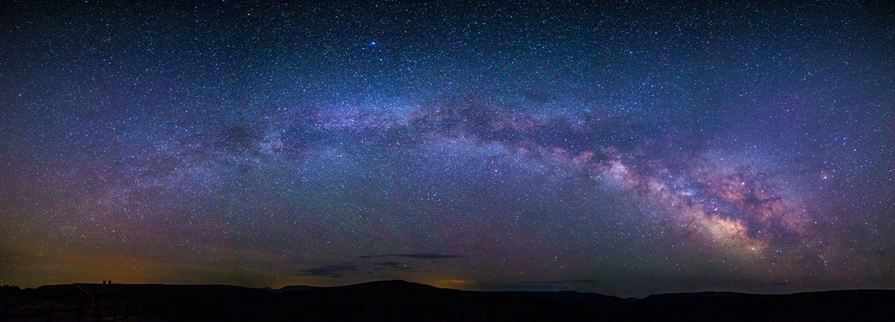 The Milky Way bends above the silhouetted horizon in this panoramic view at Black Canyon of the Gunnison National Park, CO