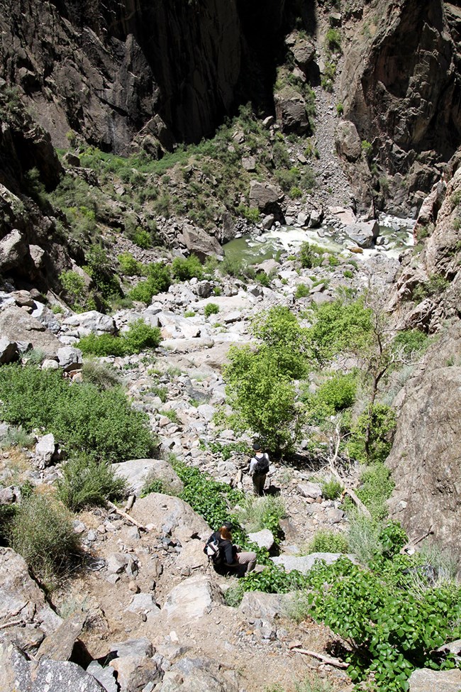 two hikers scrambling down rocky ledges with river down below