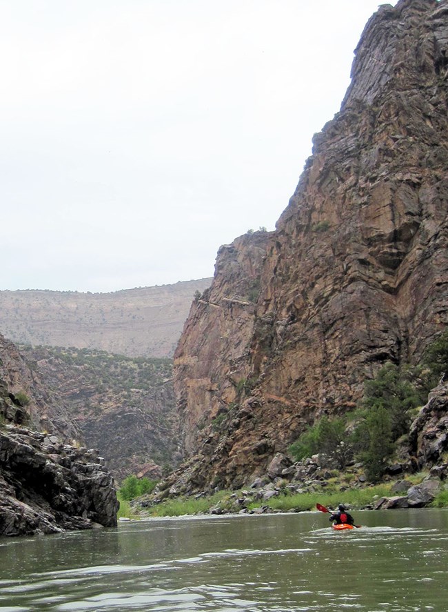 kayaker paddling on calm river water with dark canyon walls on both sides