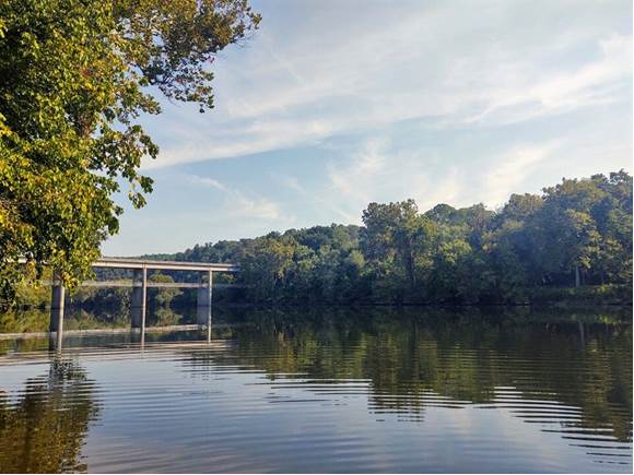View of James River Bridge with the James River passing underneath on a clear day with trees in the background.