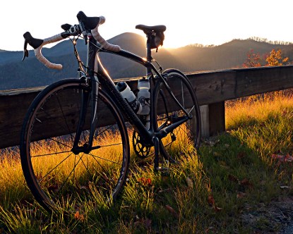 A bicycle leans against a Parkway guard rail at sunset