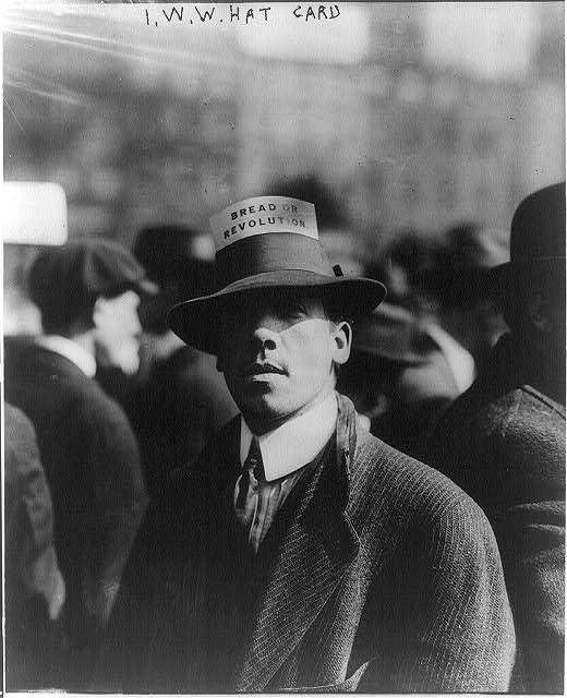 a man wearing a hat with a piece of paper that reads "bread or revolution"