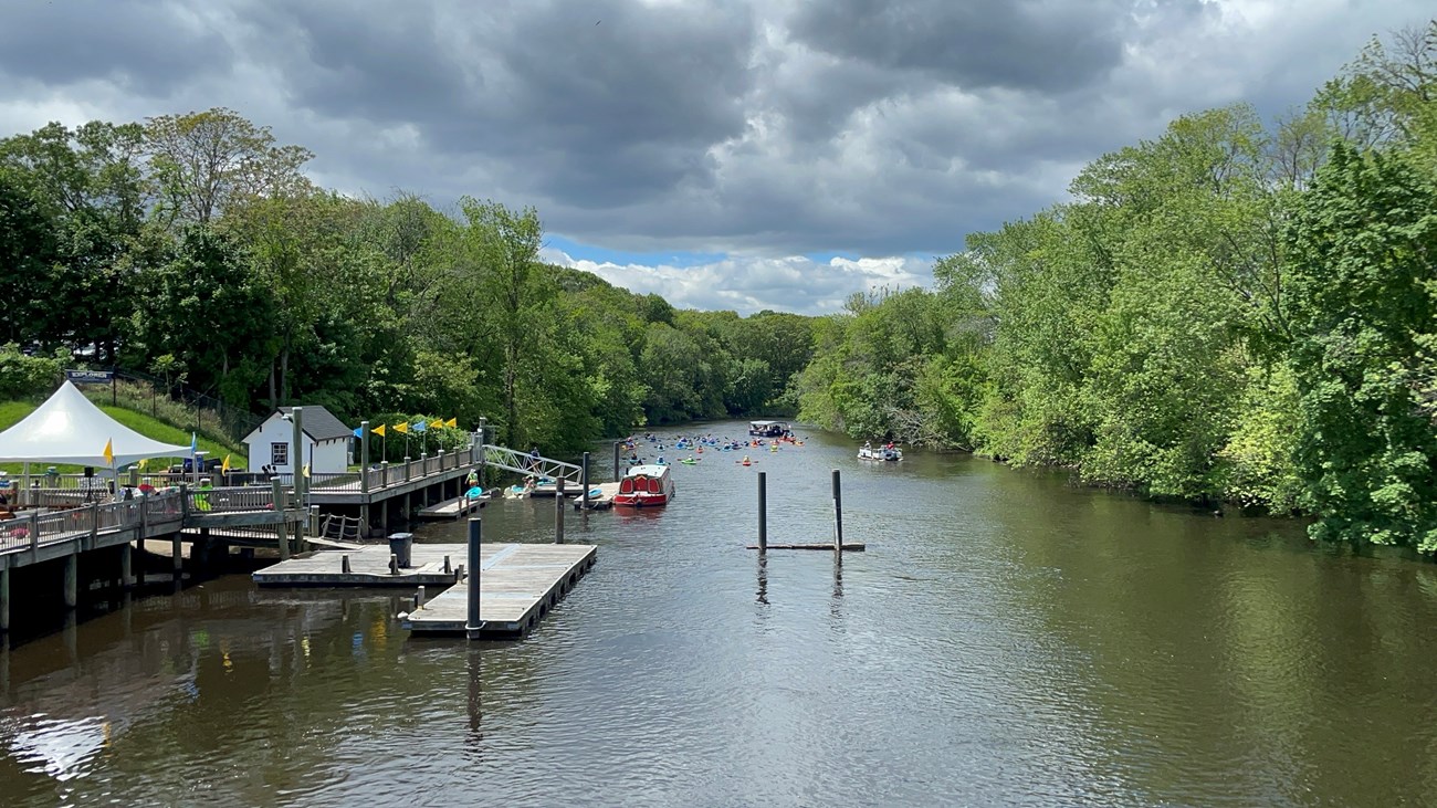 Group of kayakers on the river with boat. Docks and buildings are visible on the left