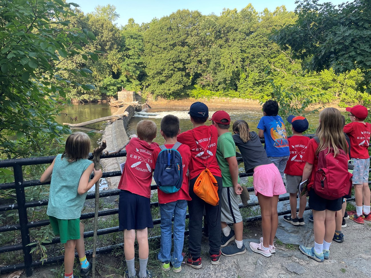 Group of children standing along a metal railing looking at a dam