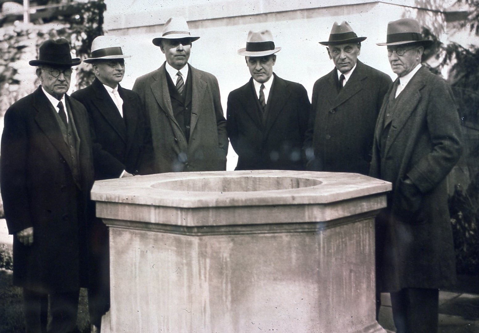 Group of men in suits and hats standing around stone well