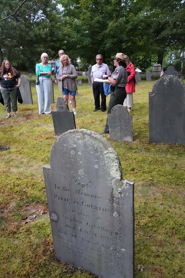 Group of visitors stand in cemetery listening to Park Ranger speak